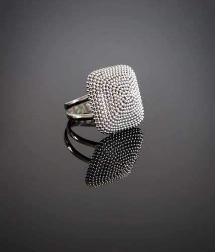 Silver square ring with textured, dotted surface reflecting on a dark background.