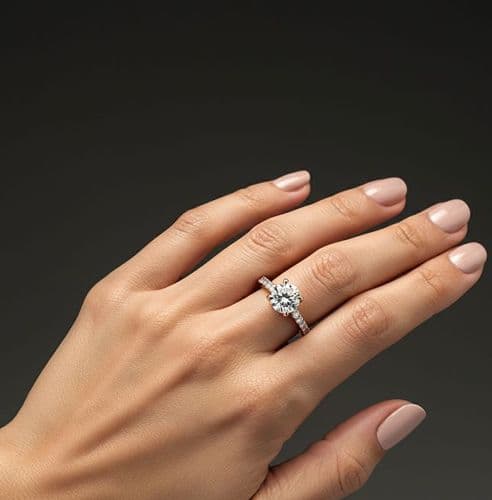 Woman's hand wearing a sparkling diamond engagement ring on her ring finger.